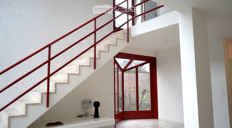 Modern hallway with white brick walls, a staircase with red metal railing, and a glass-paneled door leading outside.