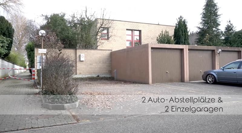 Two individual garages and two parking spaces in front of a modern building with a high wall.