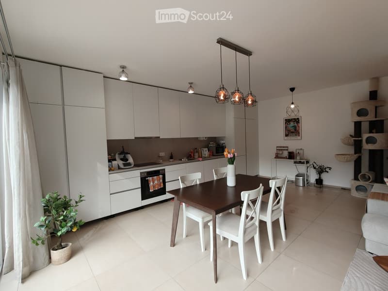 Modern kitchen and dining area with white cabinets, a dark wooden dining table, white chairs, and a cat tree in the corner.