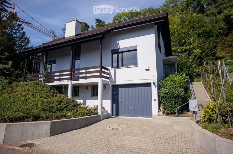Two-story modern house with white exterior, grey garage door, and raised ground floor accessed by stairs.