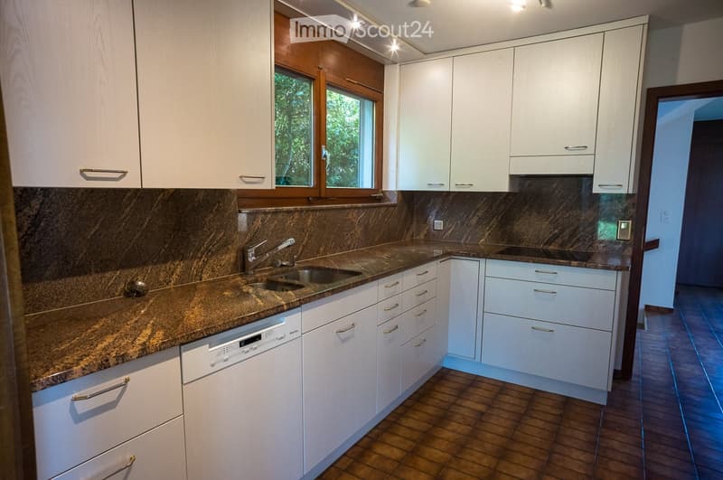 Modern kitchen with white cabinets, granite countertops, and a stainless steel sink. Features include a dishwasher, tiled floor, and large windows.
