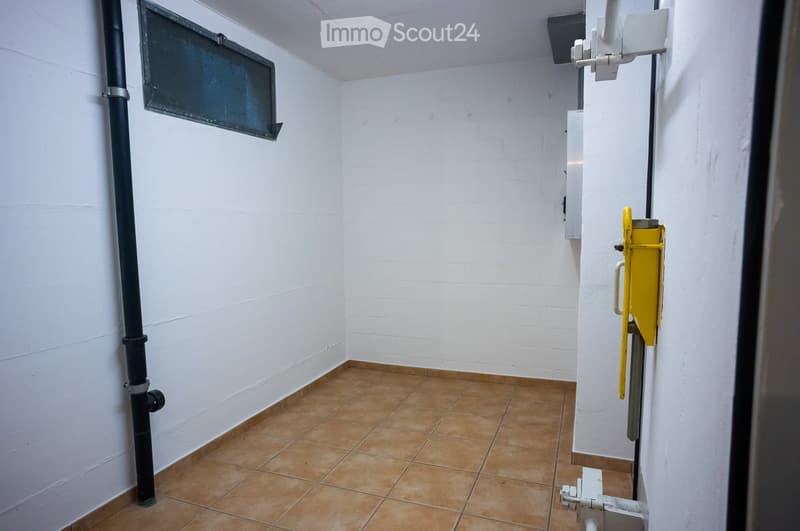 Empty room with white brick walls, brown tiled floor, and a small window with a black frame. A yellow utility box is mounted on the wall.