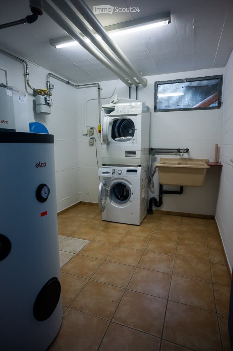 Utility room with a stacked washer and dryer, water heater, and sink.