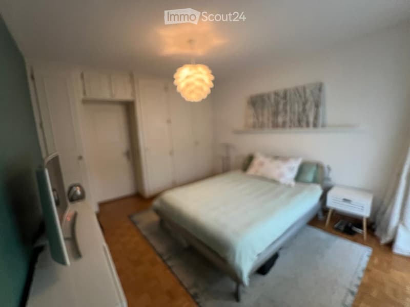 A modern bedroom with a neatly made bed, a nightstand with a lamp, a cabinet, and a picture frame on the wall.