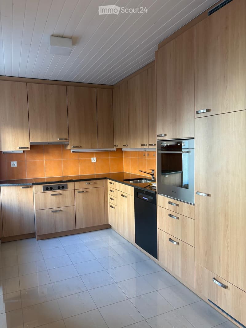 Modern kitchen with light wooden cabinets, stainless steel appliances, and a tiled backsplash.