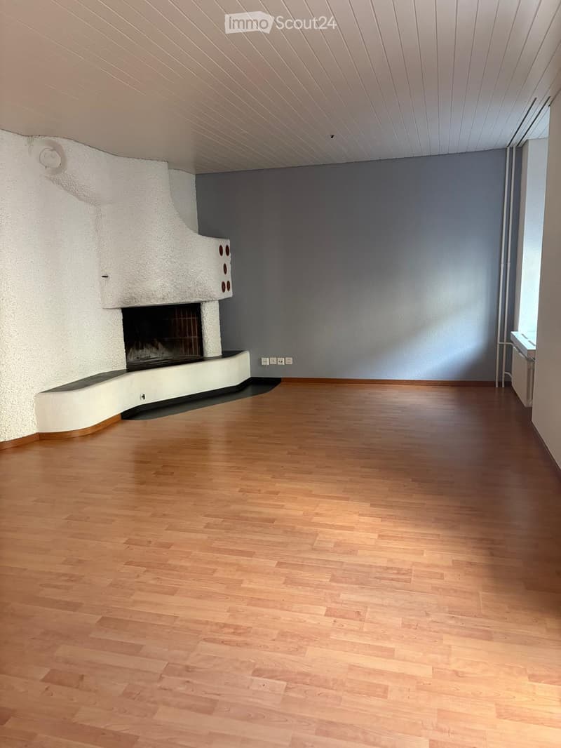 Empty room with wooden flooring, grey walls, and a built-in fireplace on the left side.
