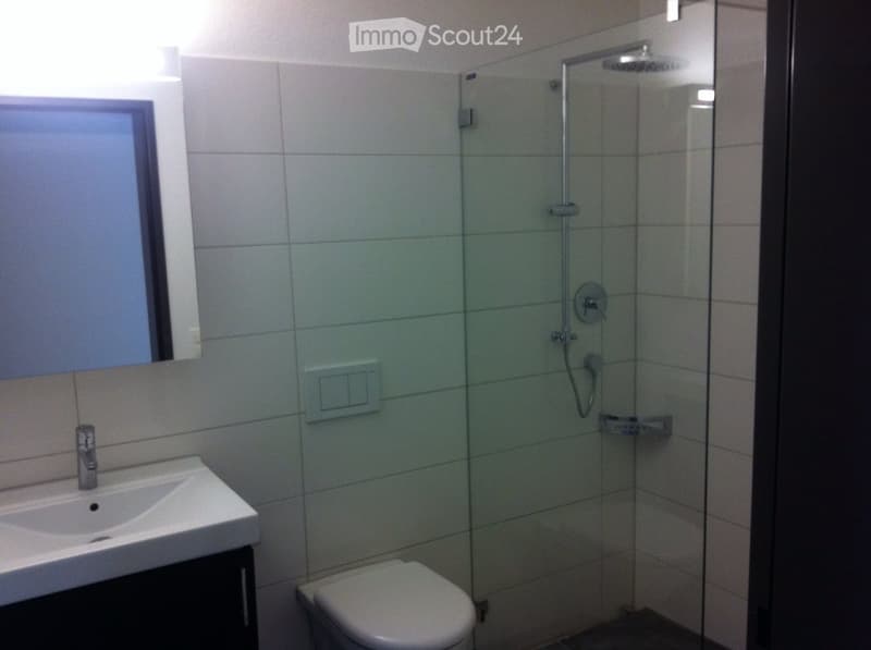 Modern bathroom with white tiles, a glass-enclosed shower, a sink with a modern faucet, and a toilet.