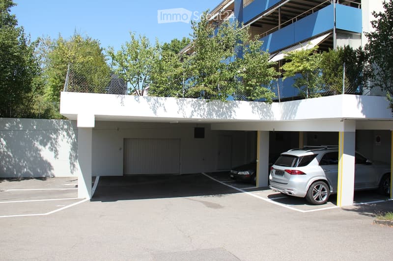 Modern multi-story building with a covered parking area, featuring two parked cars and a clean, organized space.