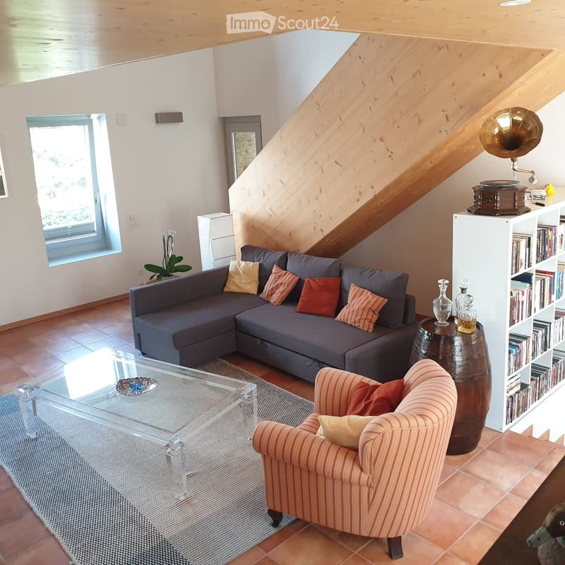 Modern living room with grey sectional sofa, striped armchair, glass coffee table, bookshelf, gramophone, and decorative vases.