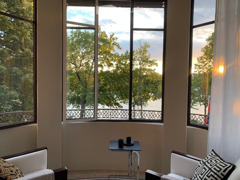 Large windows with a view of trees, balcony with decorative railings, couch, side table
