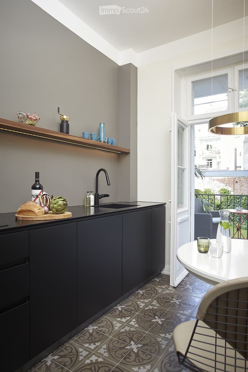 Modern kitchen with black cabinets, wooden shelves, patterned tile flooring, and a dining area with a round table and chairs