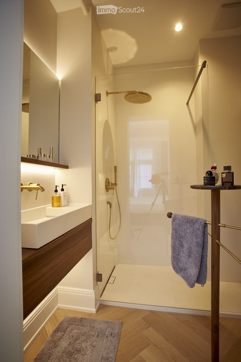 Modern bathroom with white walls, wooden vanity, glass shower enclosure, rain shower head, and towel rack