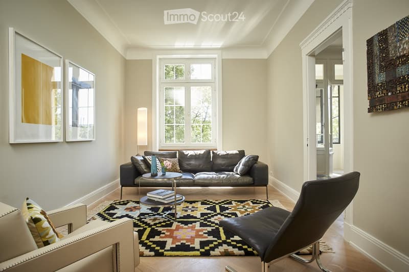 Spacious living room with large windows, hardwood floors, black leather sofa, patterned area rug, and decorative wall art