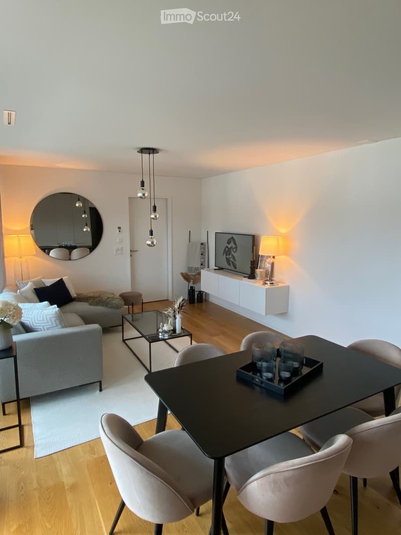 Modern living and dining area with a grey sofa, coffee table, dining table with chairs, and a television on a white console.