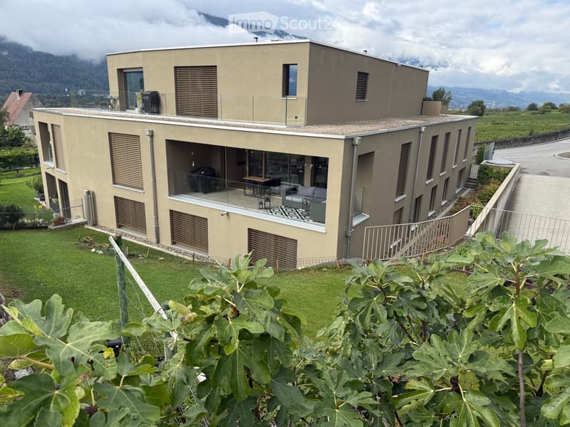 Modern two-story house with large windows, a balcony, and a well-maintained garden.