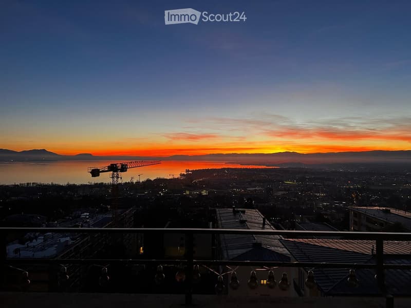 Balcony overlooking a cityscape at sunset, with a body of water and distant mountains visible.