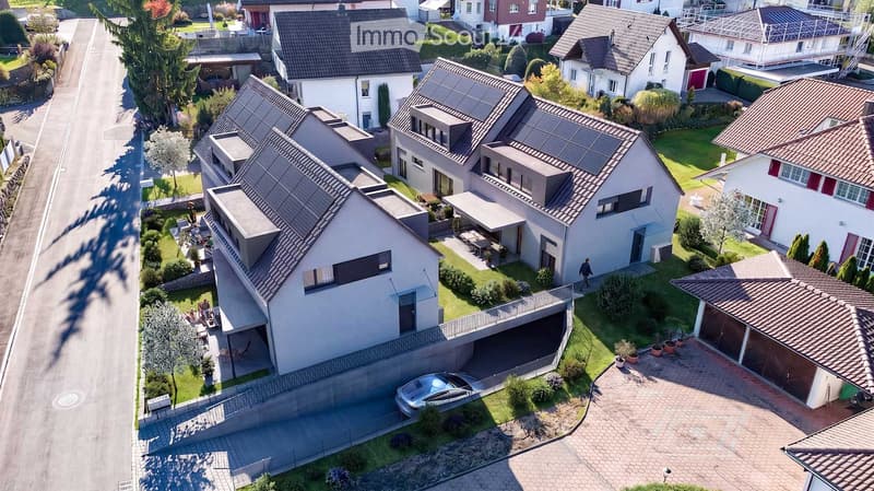 Aerial view of a residential neighborhood with multiple houses, solar panels on roofs, well-maintained gardens, and a parked car in a driveway.