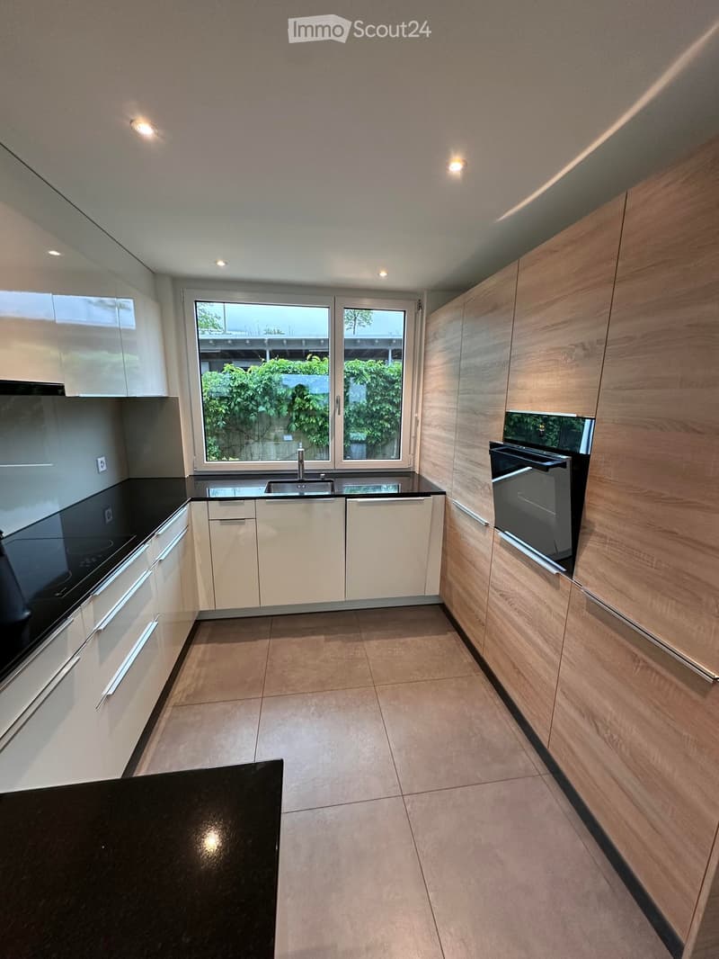 Modern kitchen with white cabinets, black countertops, and a large window overlooking greenery.