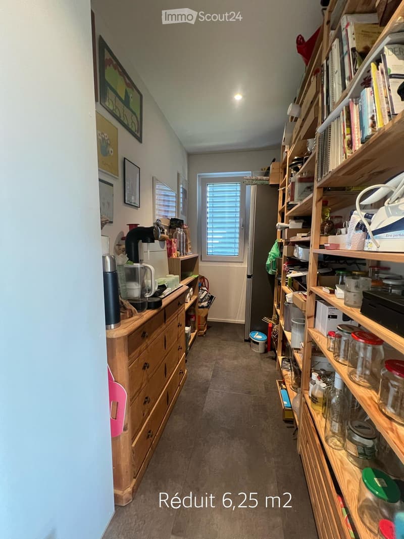 A narrow hallway with wooden shelves on the right side, a small wooden cabinet on the left, and a door leading to another room at the end.