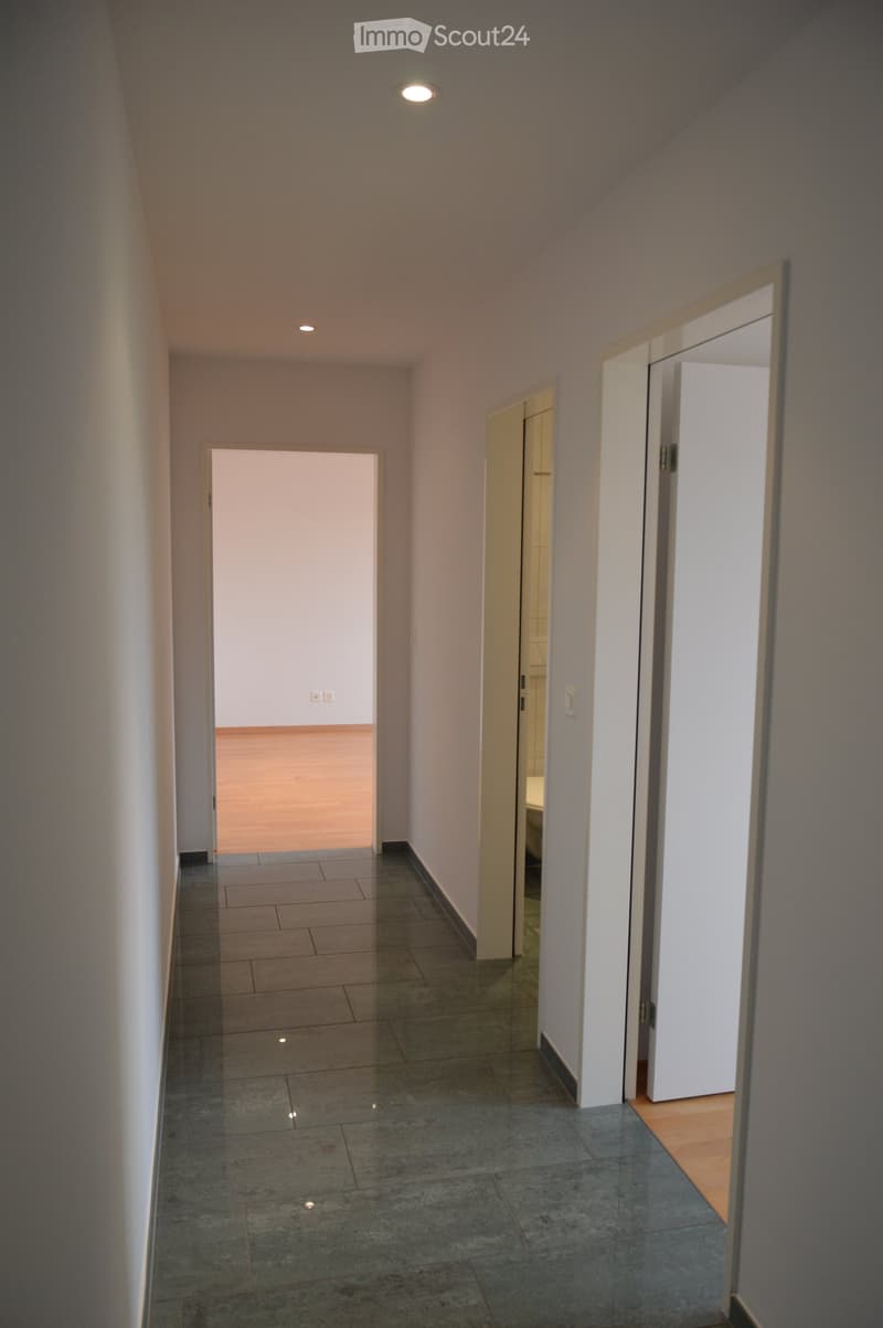 Empty hallway with tiled floor, white walls, and recessed lighting. Three doors lead to other rooms.