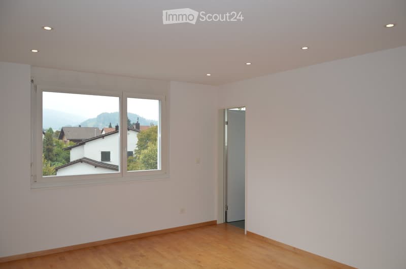 Empty room with light-colored walls, wooden flooring, and large windows offering a scenic view of the surrounding area.
