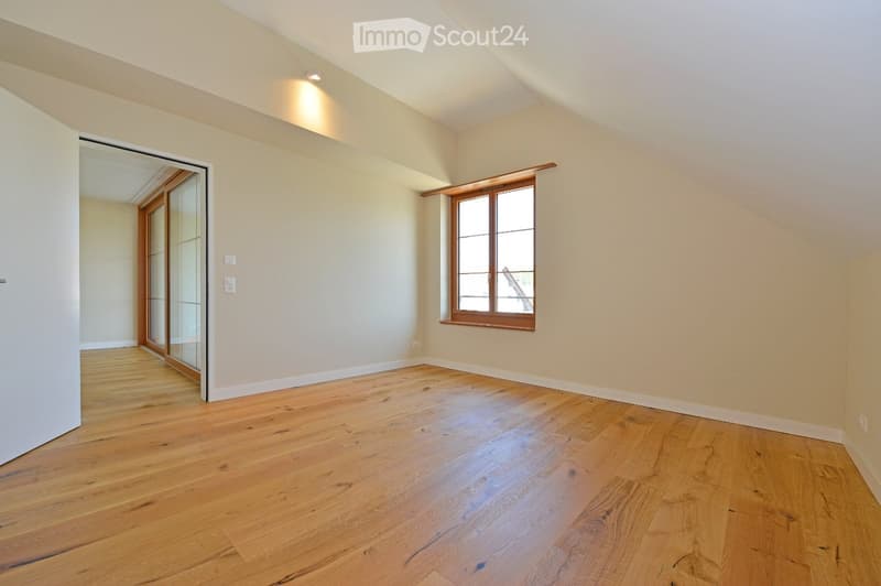 Empty room with wooden flooring, white walls, and a large window with wooden frame. The room has a sliding glass door leading to another space.