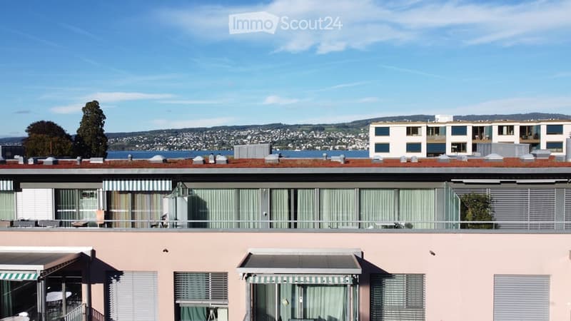 Multi-story residential building with balconies, large windows, and a scenic view of a body of water and distant cityscape.