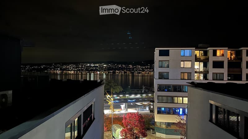 Night view of a modern apartment building with illuminated windows, overlooking a cityscape and waterfront.