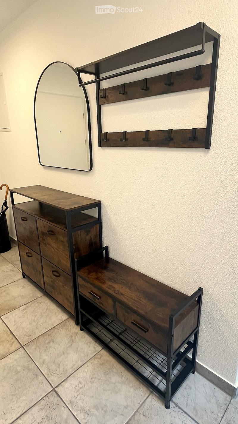 A modern hallway features a wooden bench with metal frame, a wall-mounted coat rack, and a large oval mirror.