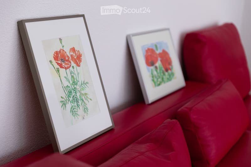 Red sofa with two framed pictures of poppies placed on it.