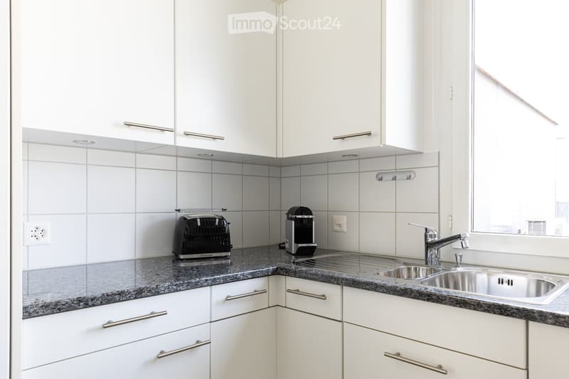 Modern kitchen with white cabinets, granite countertops, stainless steel sink, toaster, and coffee maker.