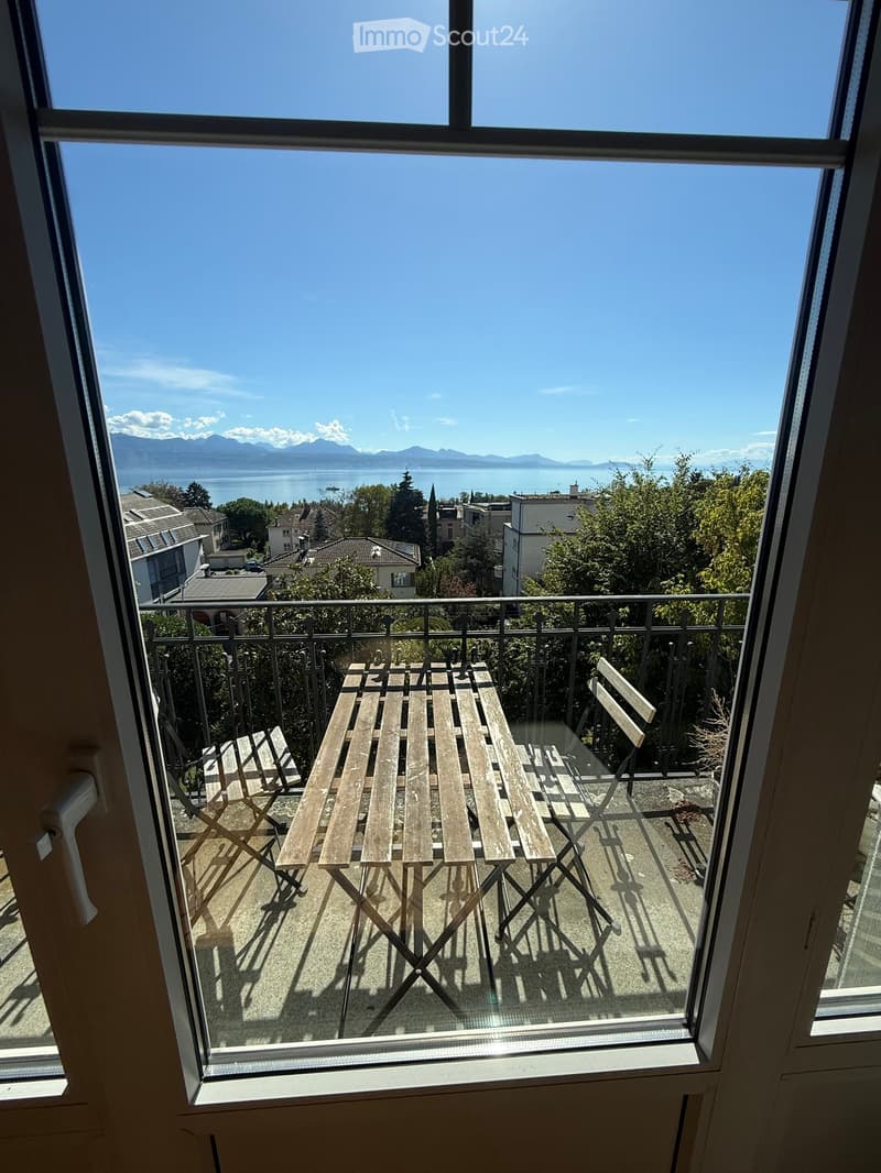 Balcony with wooden table and chairs, overlooking a scenic lake and mountains.