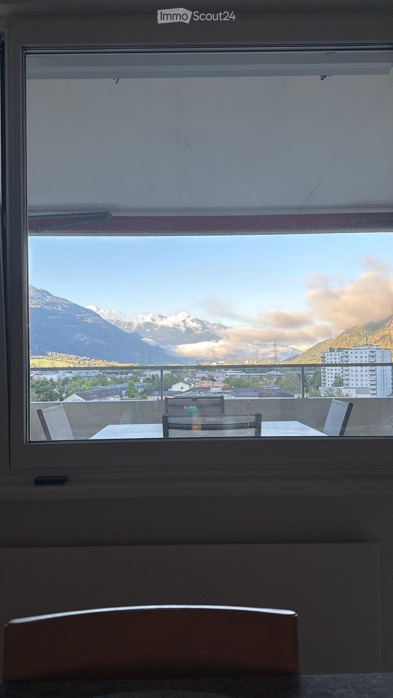 Balcony with a table and chairs, overlooking a scenic mountain view and cityscape.