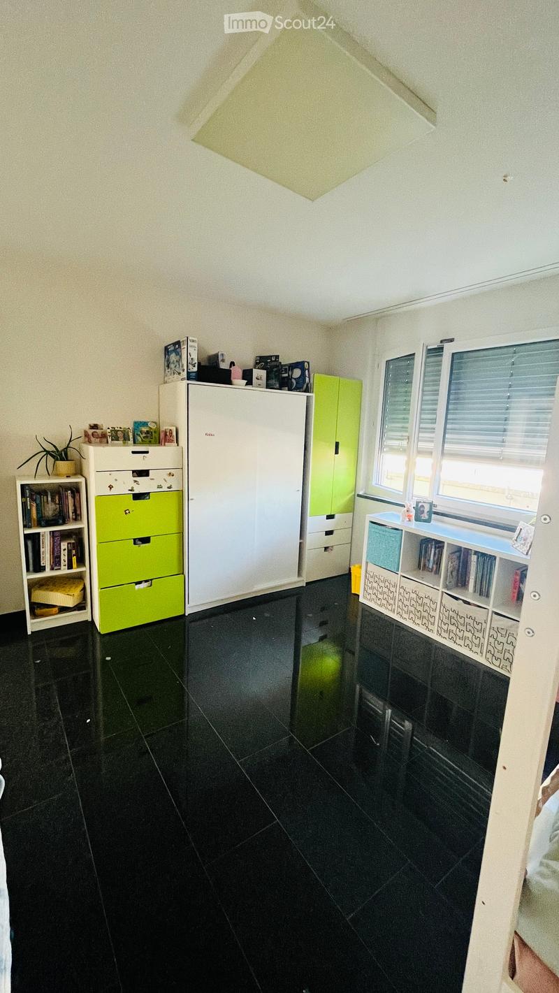 A well-organized room with black tiled flooring, white and green cabinets, a bookshelf, and a small plant on a shelf.
