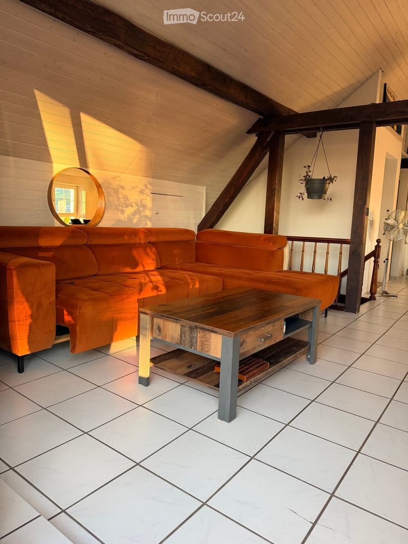 Living room with a large orange sectional sofa, wooden coffee table, round mirror, and a fan in the corner.