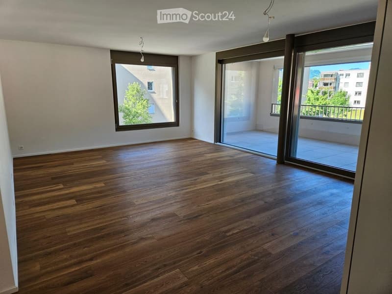Empty room with wooden flooring, large windows, and sliding glass doors leading to a balcony.