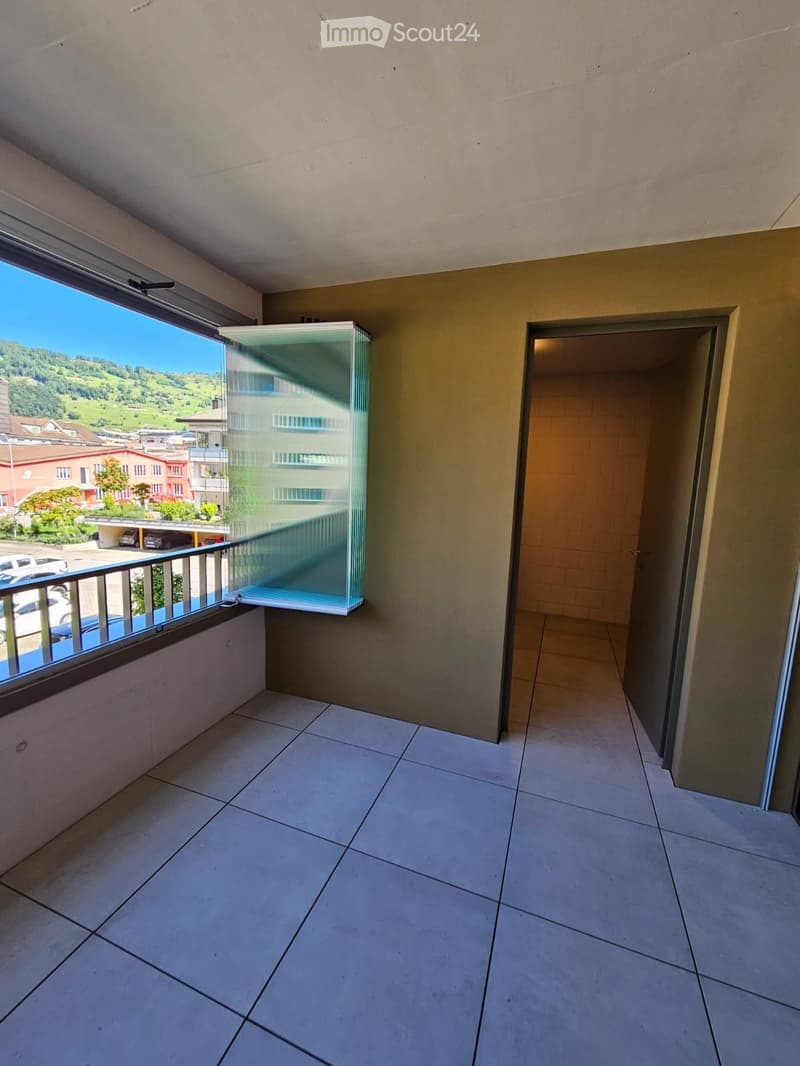 Balcony with tiled floor, large window offering a scenic view of the surrounding landscape, and a door leading to the interior.