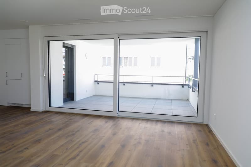 Empty room with wooden flooring, white walls, and large sliding glass doors leading to a balcony.