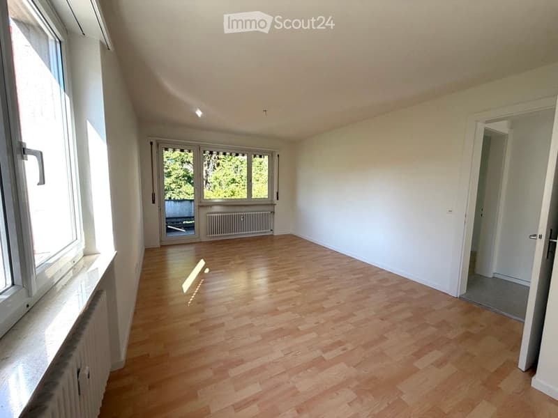 Empty room with wooden flooring, white walls, large windows, and a radiator. No furniture or equipment present.