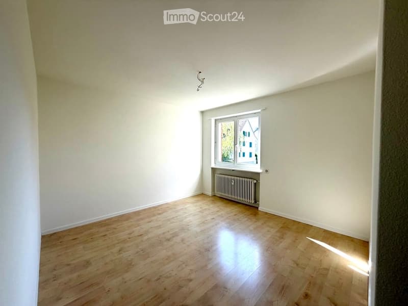 Empty room with wooden flooring, white walls, and a single window with a radiator below it.