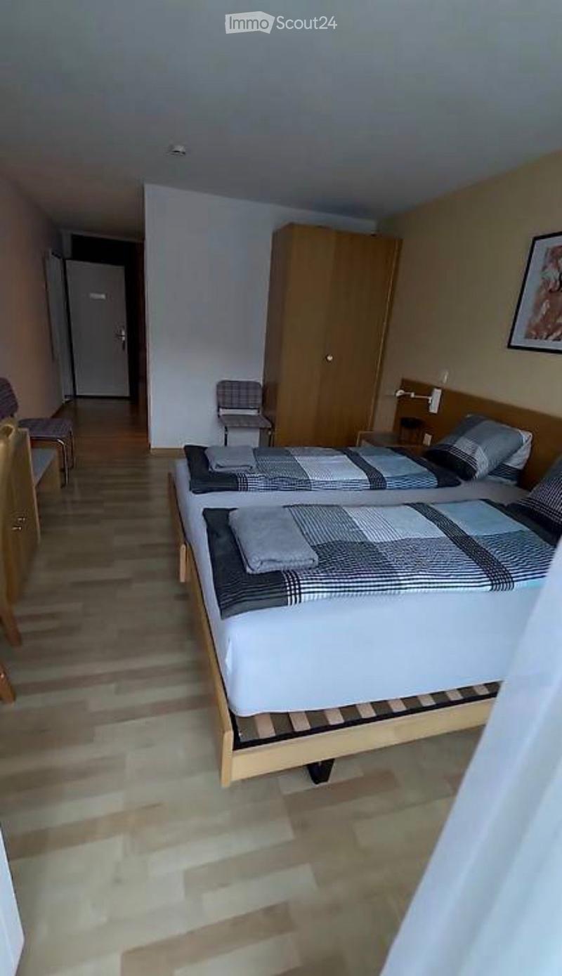 Cozy bedroom with two single beds, a wooden wardrobe, and a small chair near the door.