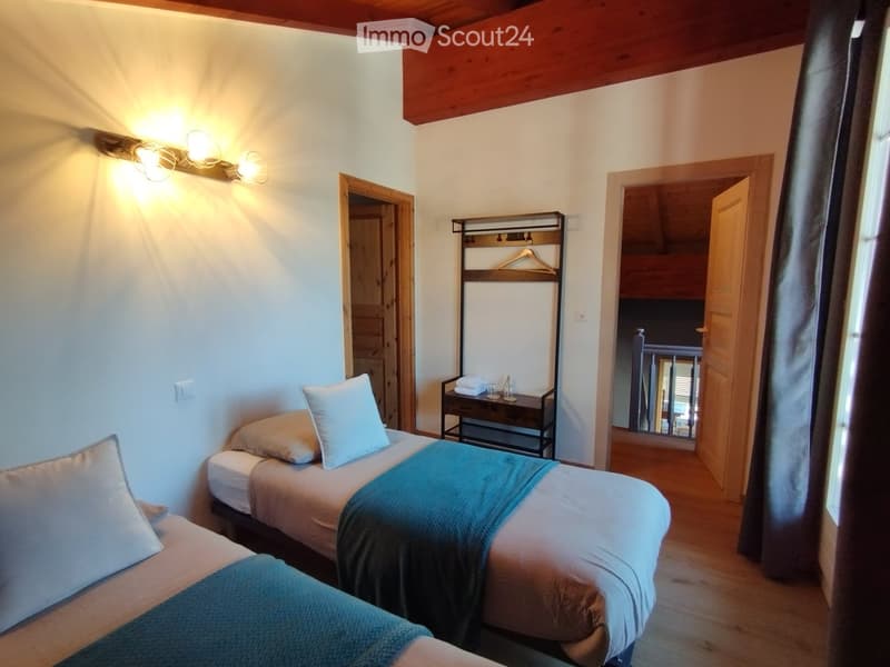 Cozy bedroom with two single beds, pillows, blankets, a nightstand with a hanger and cups, and warm lighting.