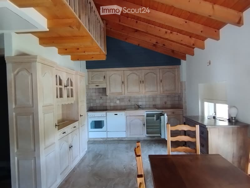 Bright kitchen with white cabinets, wooden ceiling beams, and a dining area with a table and chairs.