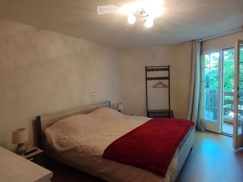 Cozy bedroom with a large bed, red blanket, nightstands with lamps, and a clothes hanger near the sliding glass door leading to a balcony.