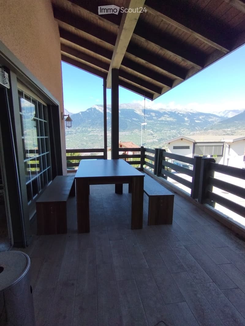 Balcony with wooden table and benches, overlooking a mountain view.