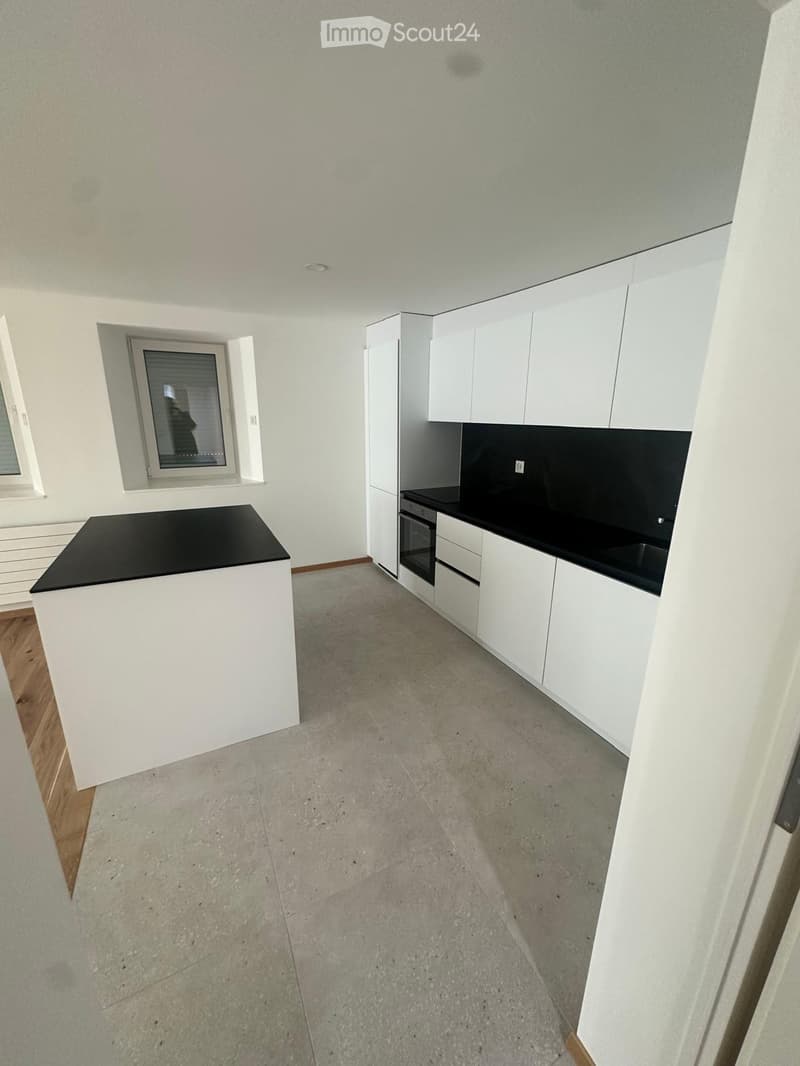 Empty kitchen with white cabinets, black countertops, and concrete flooring. No appliances or furniture are present.