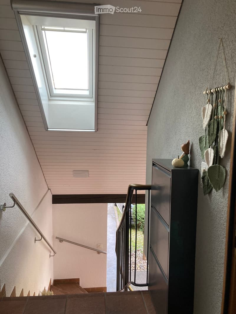 Staircase with wooden steps, metal railing, and a skylight window at the top. A small black cabinet with decorative items sits on the right side.