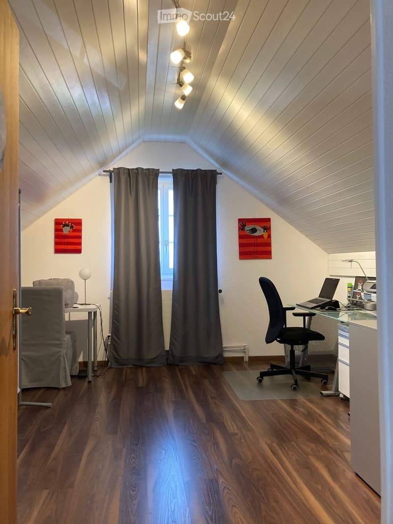 Cozy attic room with wooden floors, slanted ceilings, and modern furnishings including a desk, chair, laptop, and artwork.