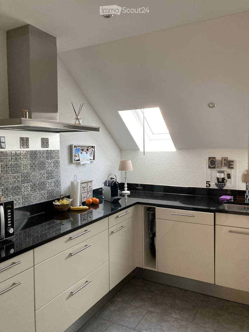 Modern kitchen with light-colored cabinets, black countertops, and a skylight window. Includes a microwave, coffee maker, sink, and decorative items.