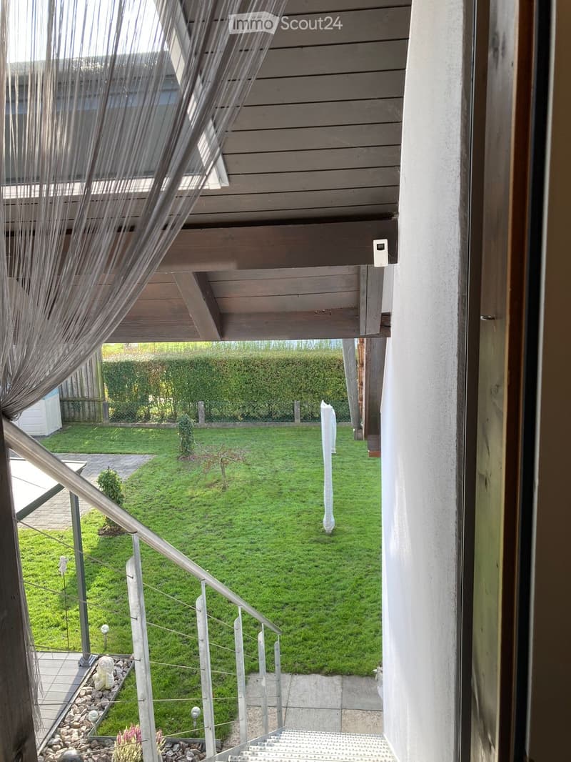 Balcony with wooden decking, metal railing, and view of a well-maintained lawn and garden area.
